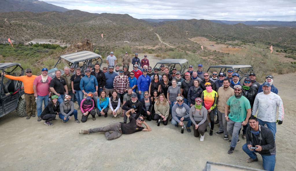 A group of over 60 construction professionals pose for a group photo in front of their UTVs overlooking a beautiful mountain vista in Black Canyon, AZ. 